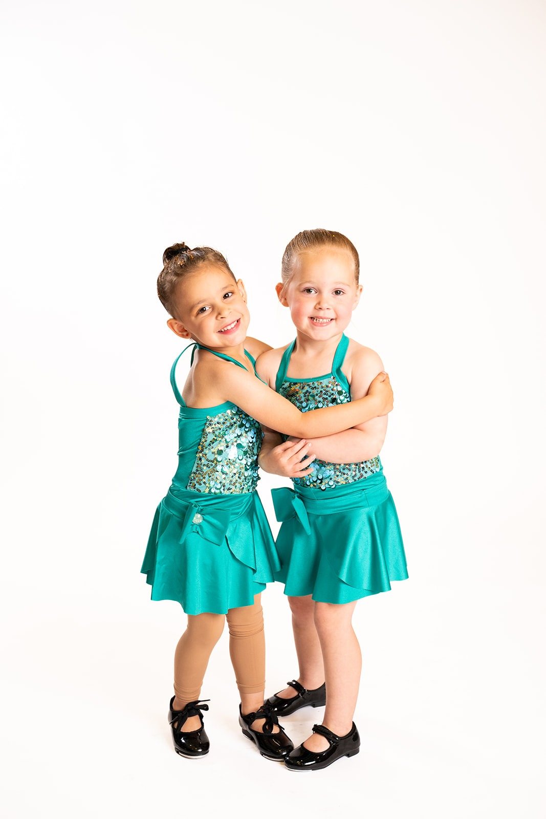 Two young dancers in teal costumes smiling and hugging