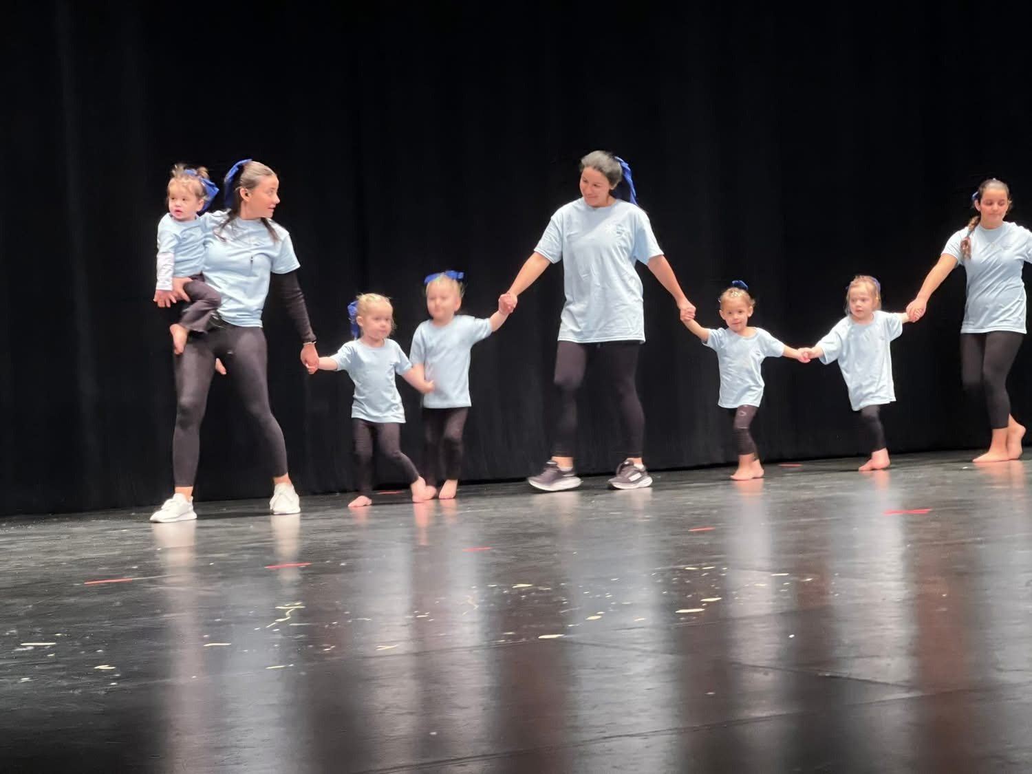 Teachers holding hands with very young dancers during a stage performance