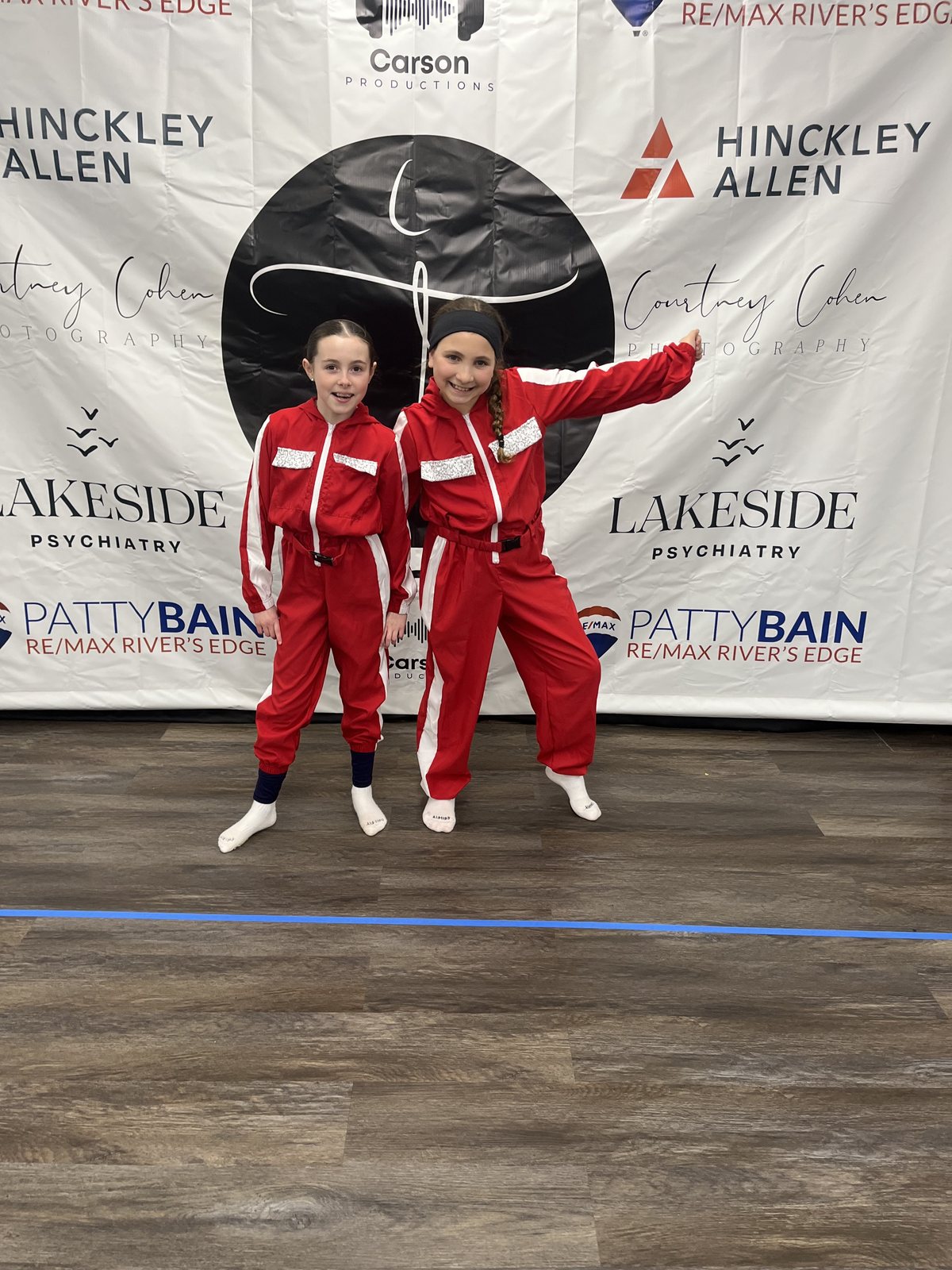 Two dancers in matching red costumes smiling together after a performance